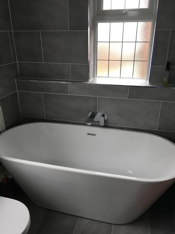 Completed bathroom installation with freestanding bath and grey tile walls
