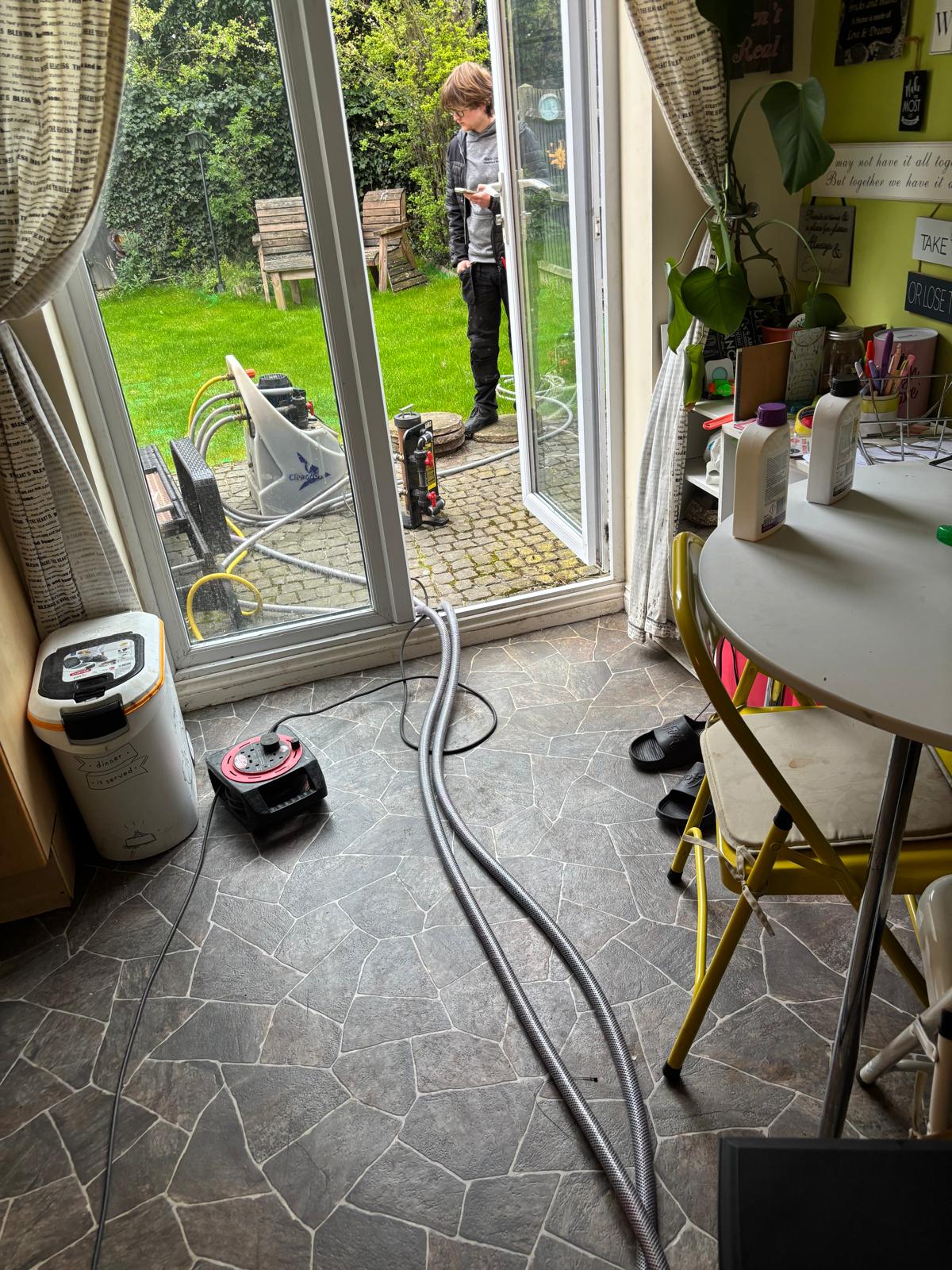 Power flush hoses routed through patio doors from the Kamco pump outside into the heating system indoors